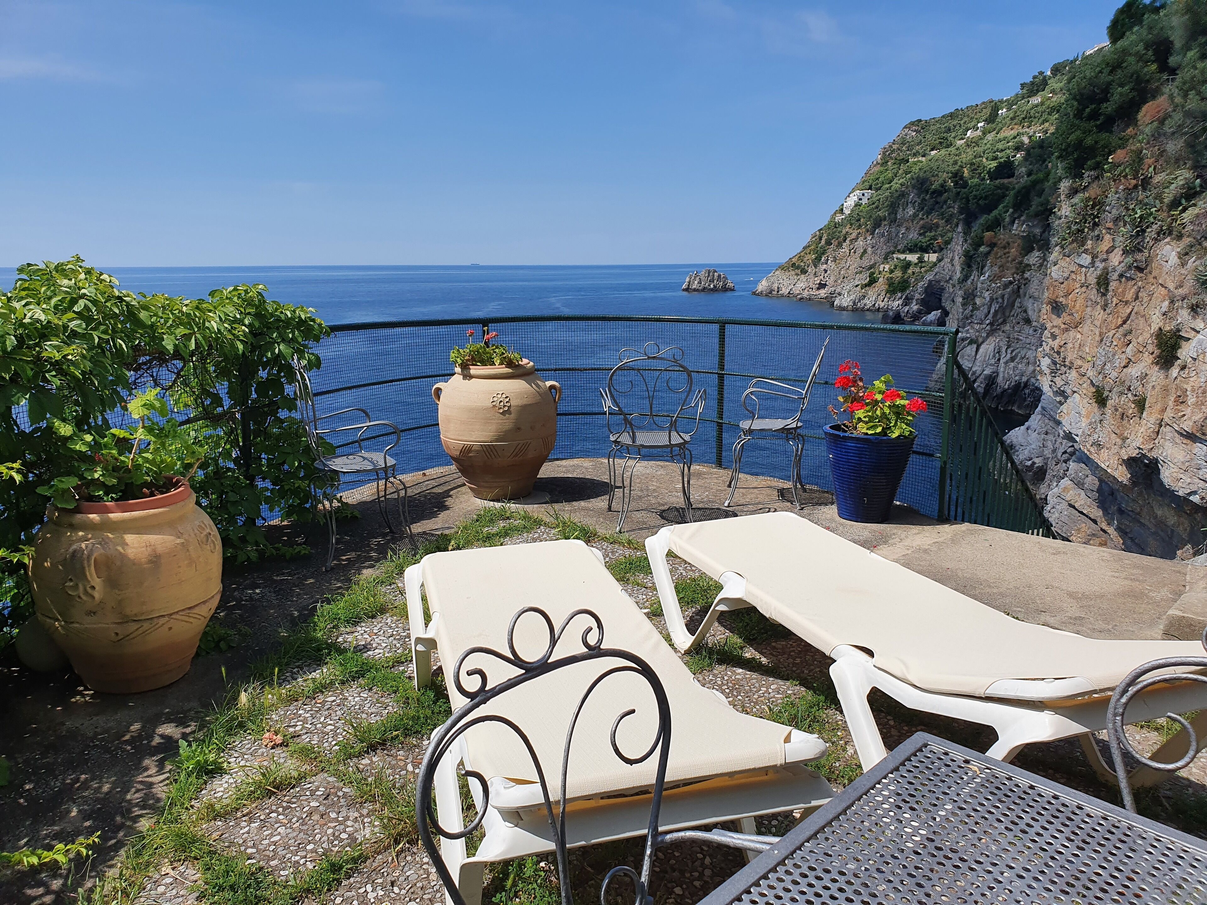 A terrace with lounge chairs, potted plants, and a view of the sea.