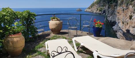A terrace with lounge chairs, potted plants, and a view of the sea.