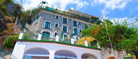 A multi-story stone building with balconies, arched windows, and outdoor seating areas.