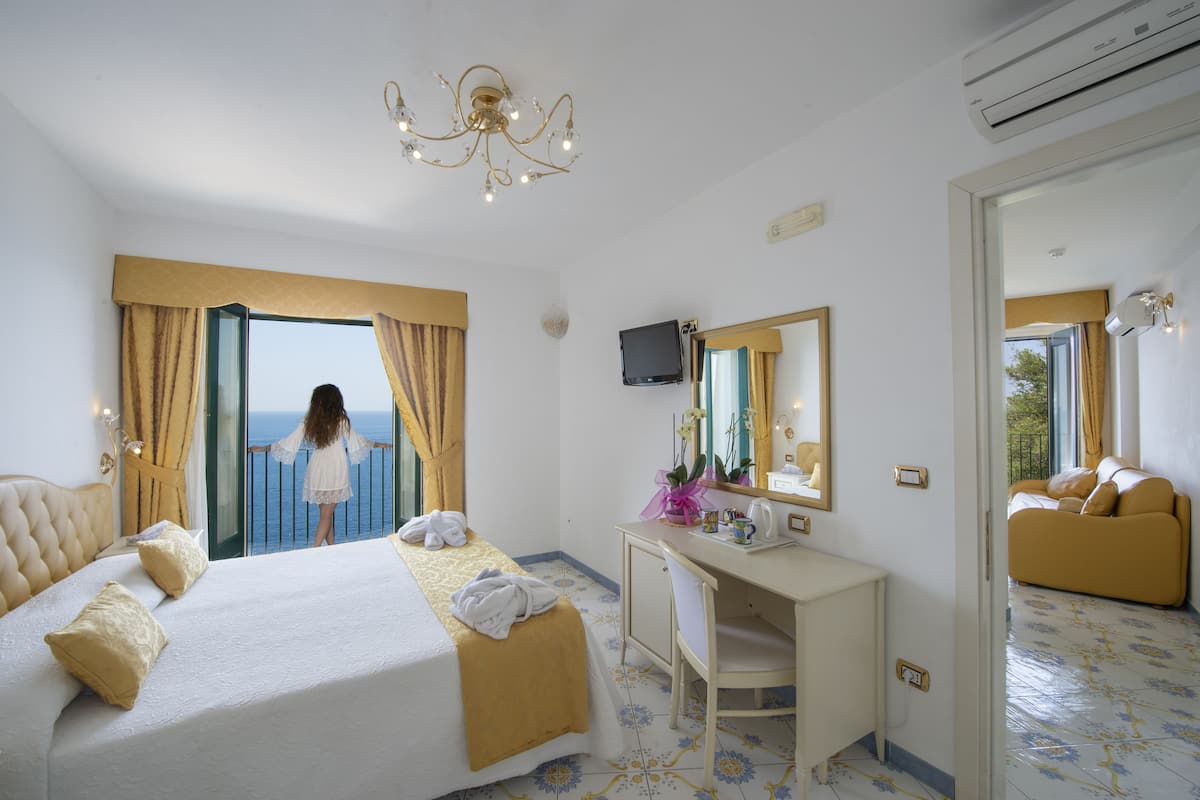 Une chambre d’hôtel avec un lit, un bureau, une chaise, une télévision et une vue sur la mer.