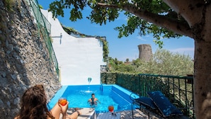 En udendørs swimmingpool med en stenvæg, en bænk og udsigt til et slot i baggrunden.