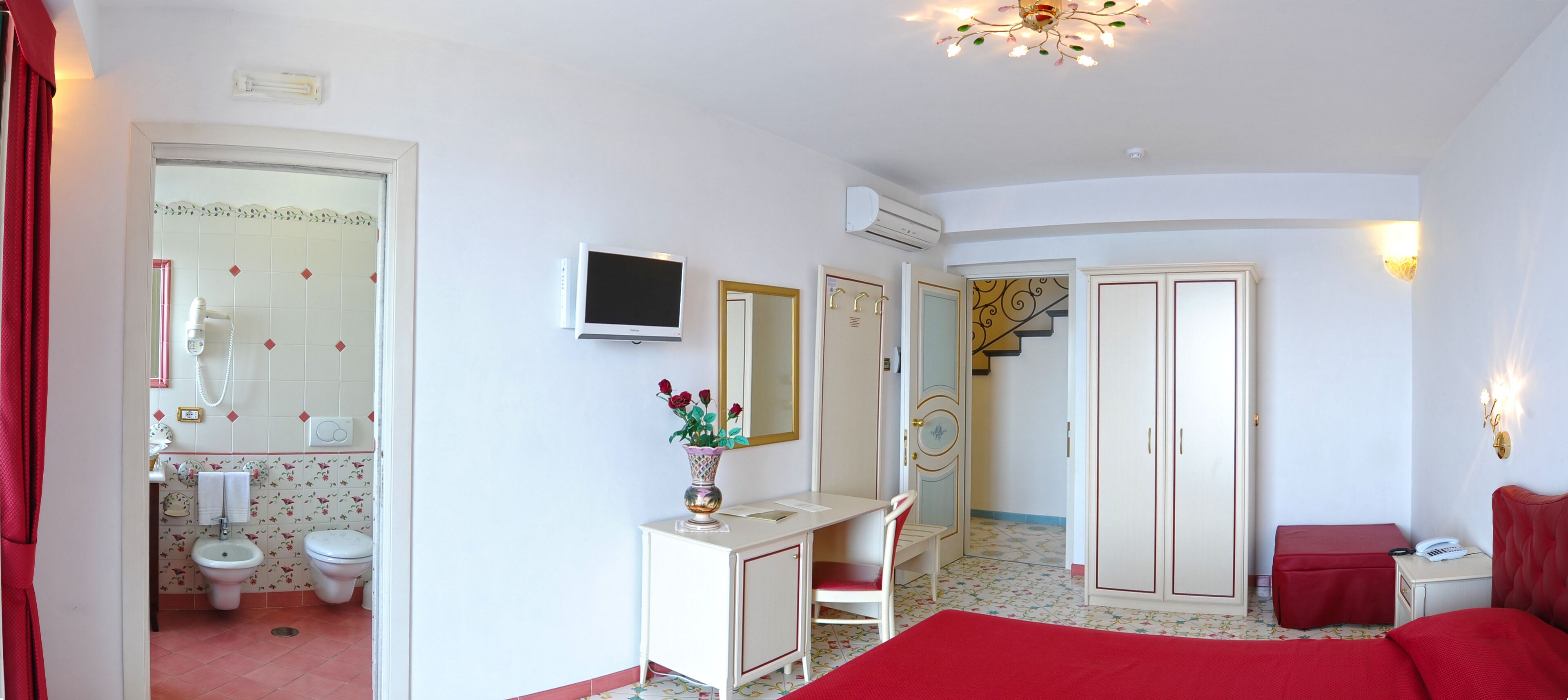 A bedroom with a bed, a desk, a chair, a TV, and a bathroom with a toilet and bidet.