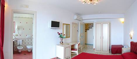 A bedroom with a bed, a desk, a chair, a TV, and a bathroom with a toilet and bidet.