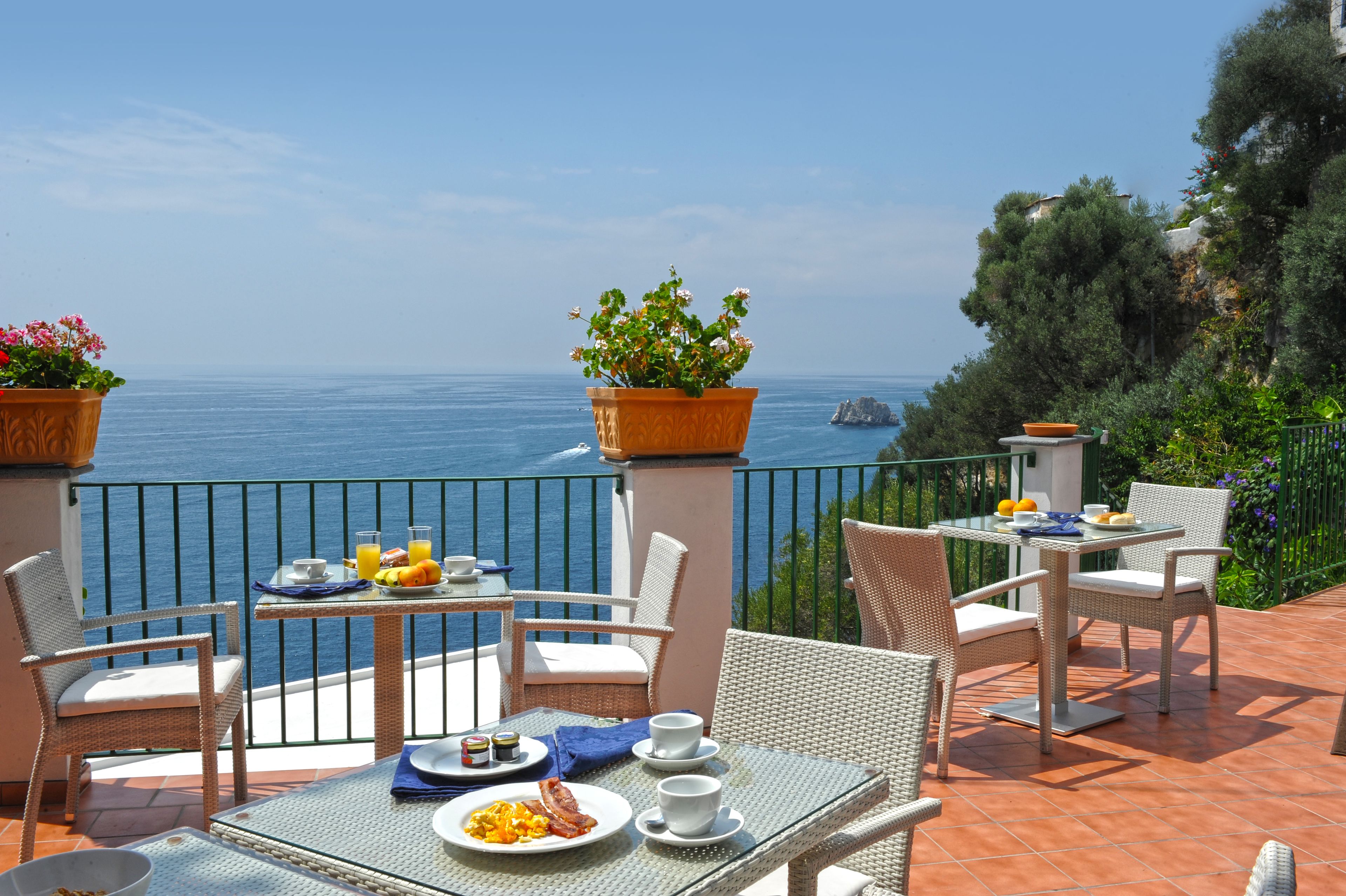 Una terraza con mobiliario de mimbre, una mesa preparada para el desayuno y vistas al mar.