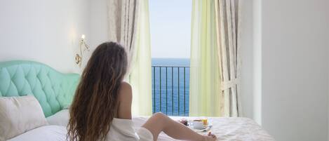 A person sitting on a bed with a view of the sea through a balcony.