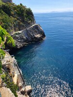 Vista costera con una escalera que desciende al mar, rodeada de terreno rocoso y vegetación.