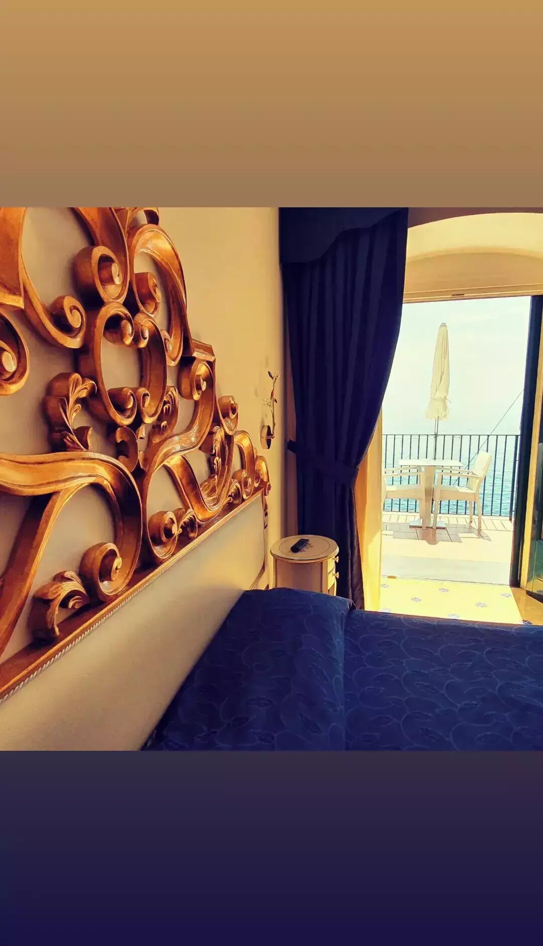 Une chambre avec un lit, un élément décoratif mural, une petite table ronde avec une chaise, et une vue sur la mer depuis un balcon.