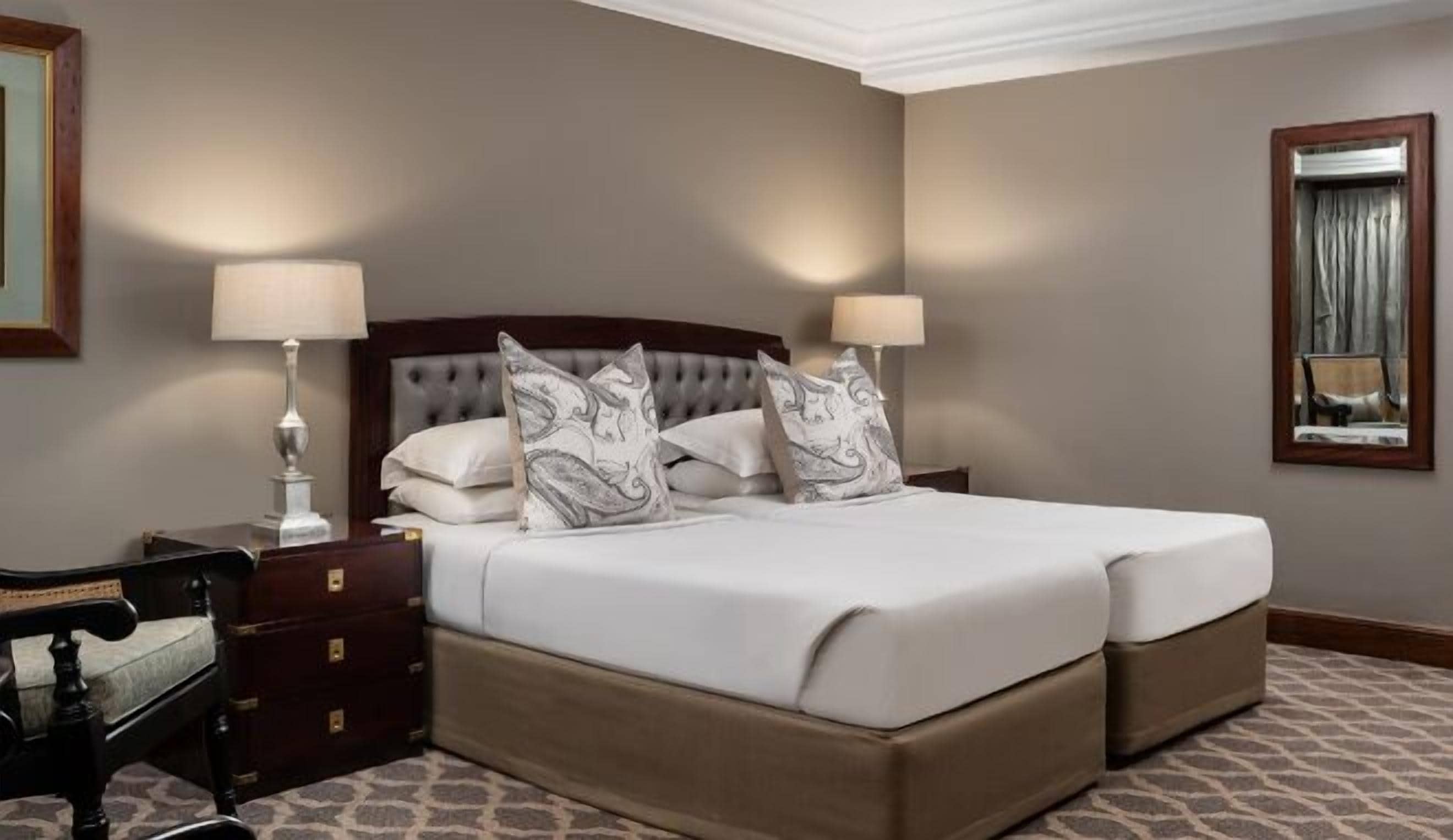 Una habitación de hotel con una cama grande, dos lámparas de noche, una mesita de madera y un espejo en la pared.
