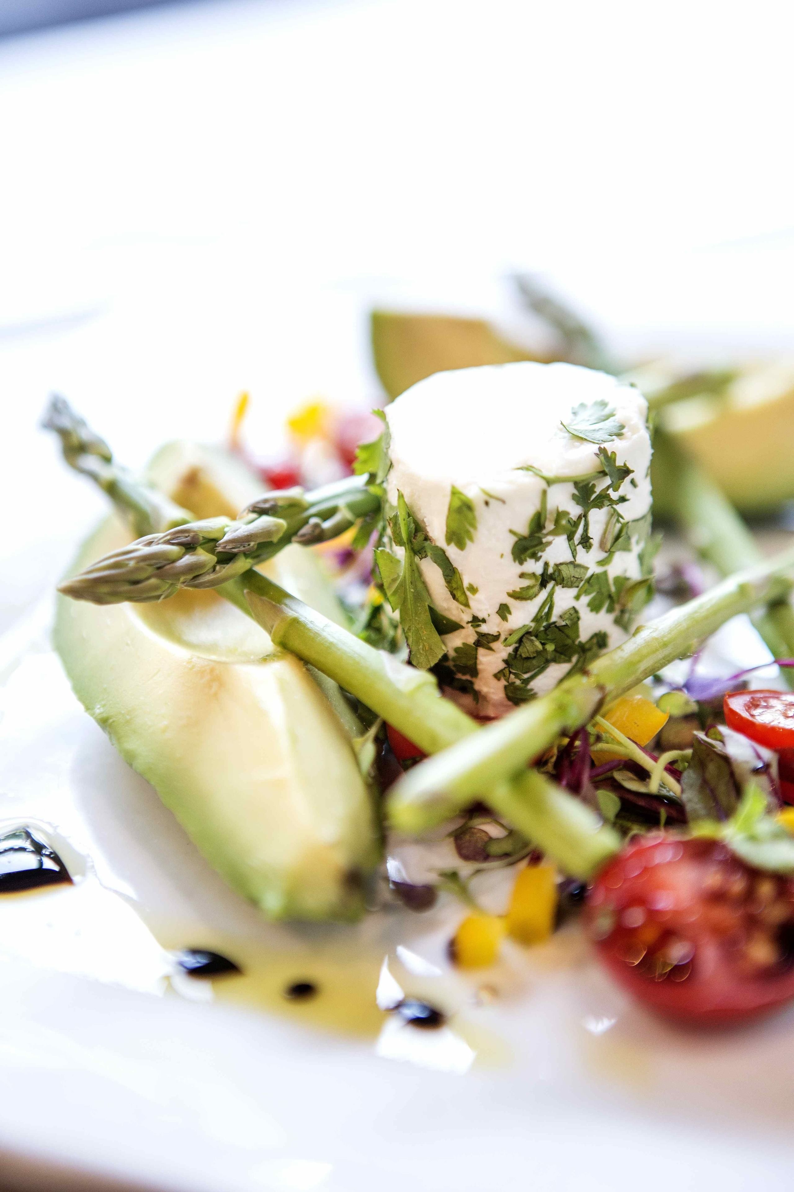 A dish with a cylindrical white object surrounded by asparagus, tomatoes, and greens.