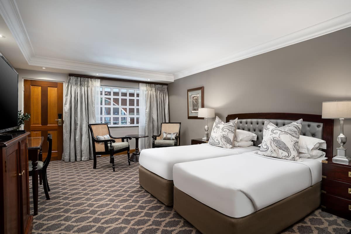 Een hotelkamer met twee bedden, een bureau, een stoel, een televisie en een raam met gordijnen.