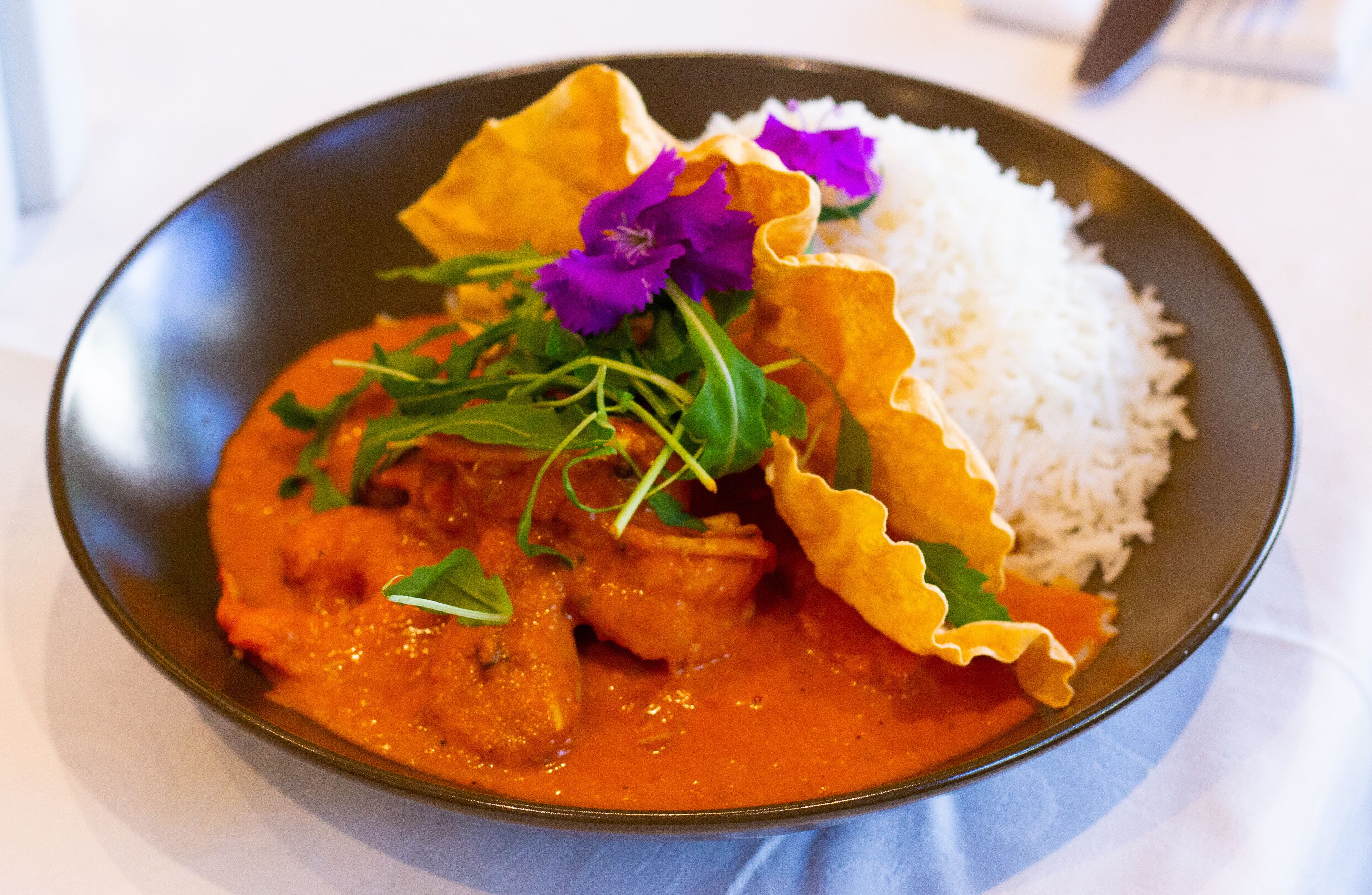 Un plato de comida con arroz y un curry, decorado con flores moradas y vegetales verdes.