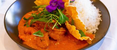 Un plato de comida con arroz y un curry, decorado con flores moradas y vegetales verdes.