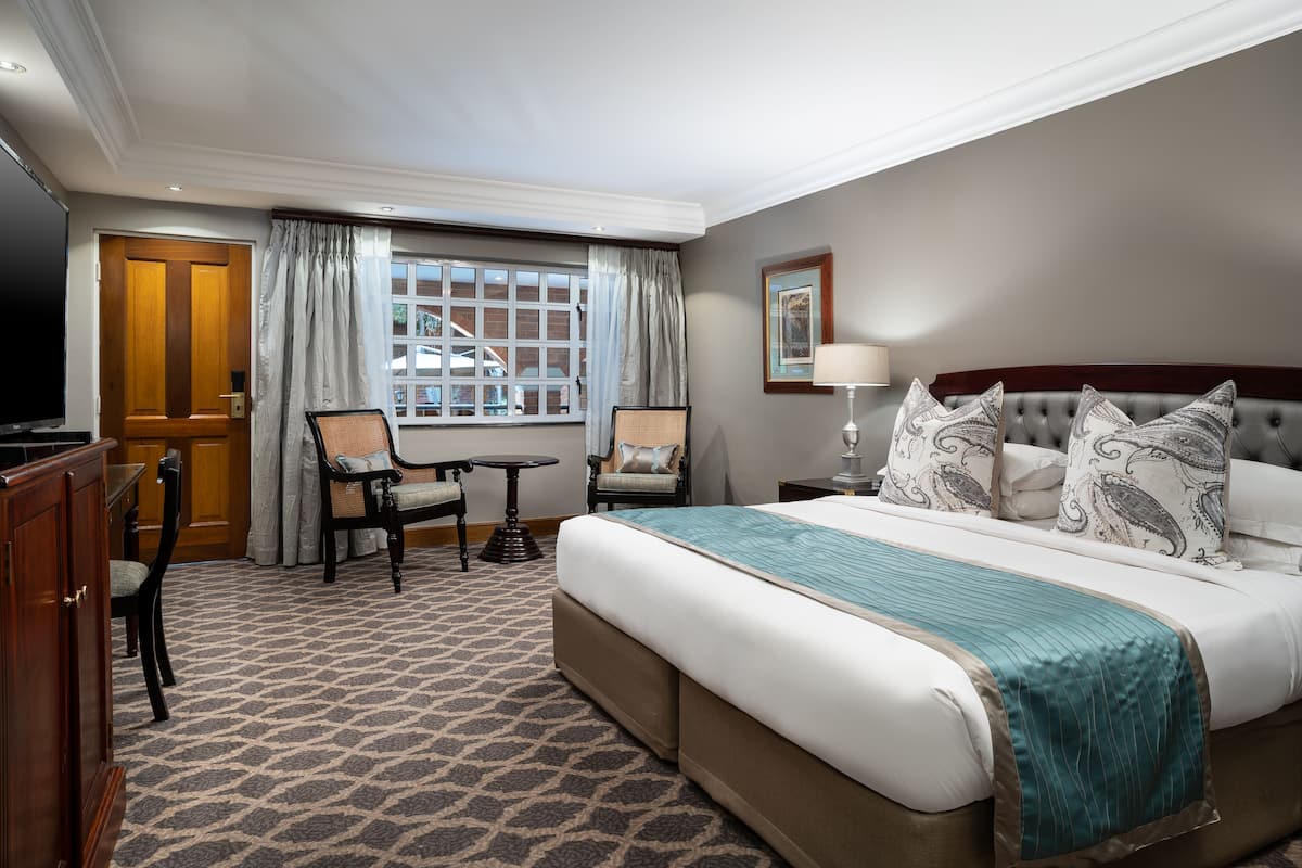 Een hotelkamer met een groot bed, twee stoelen, een tafeltje, een televisie en een raam met gordijnen.