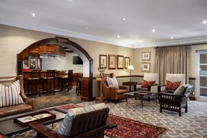 Amplia sala de estar con sofás de cuero, una mesa de centro y un tapete estampado. Cuenta con una zona de bar con taburetes y un arco de madera.