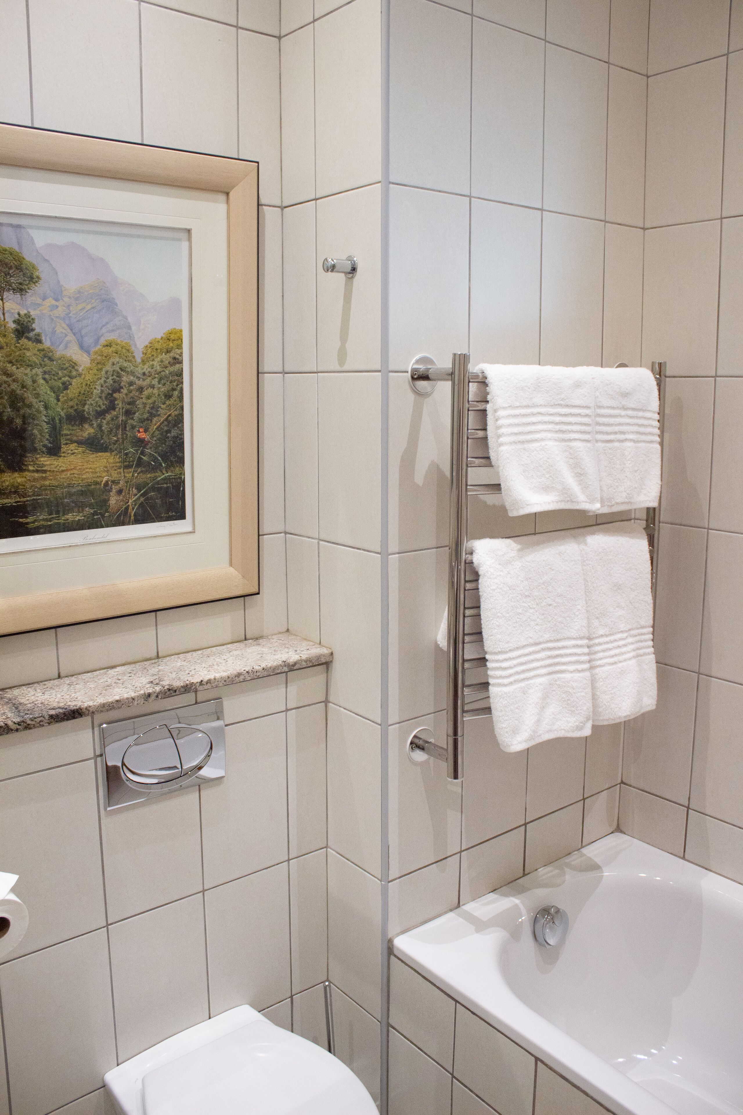 A bathroom with a bathtub, a shower, and a toilet. There is a framed picture on the wall and a towel rack with towels.
