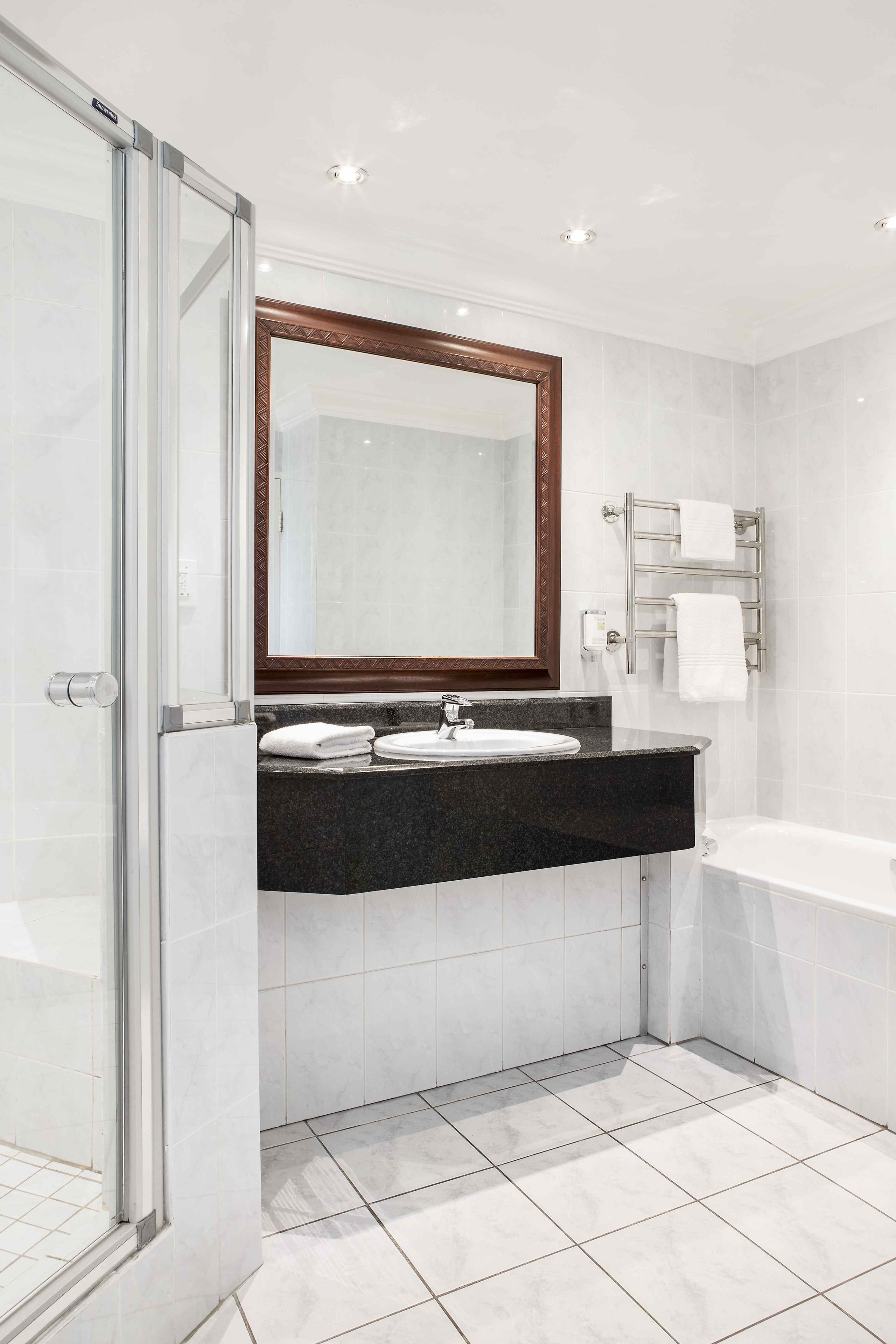 A modern bathroom with a glass shower enclosure, a sink with a dark countertop, a large mirror, and a white bathtub.