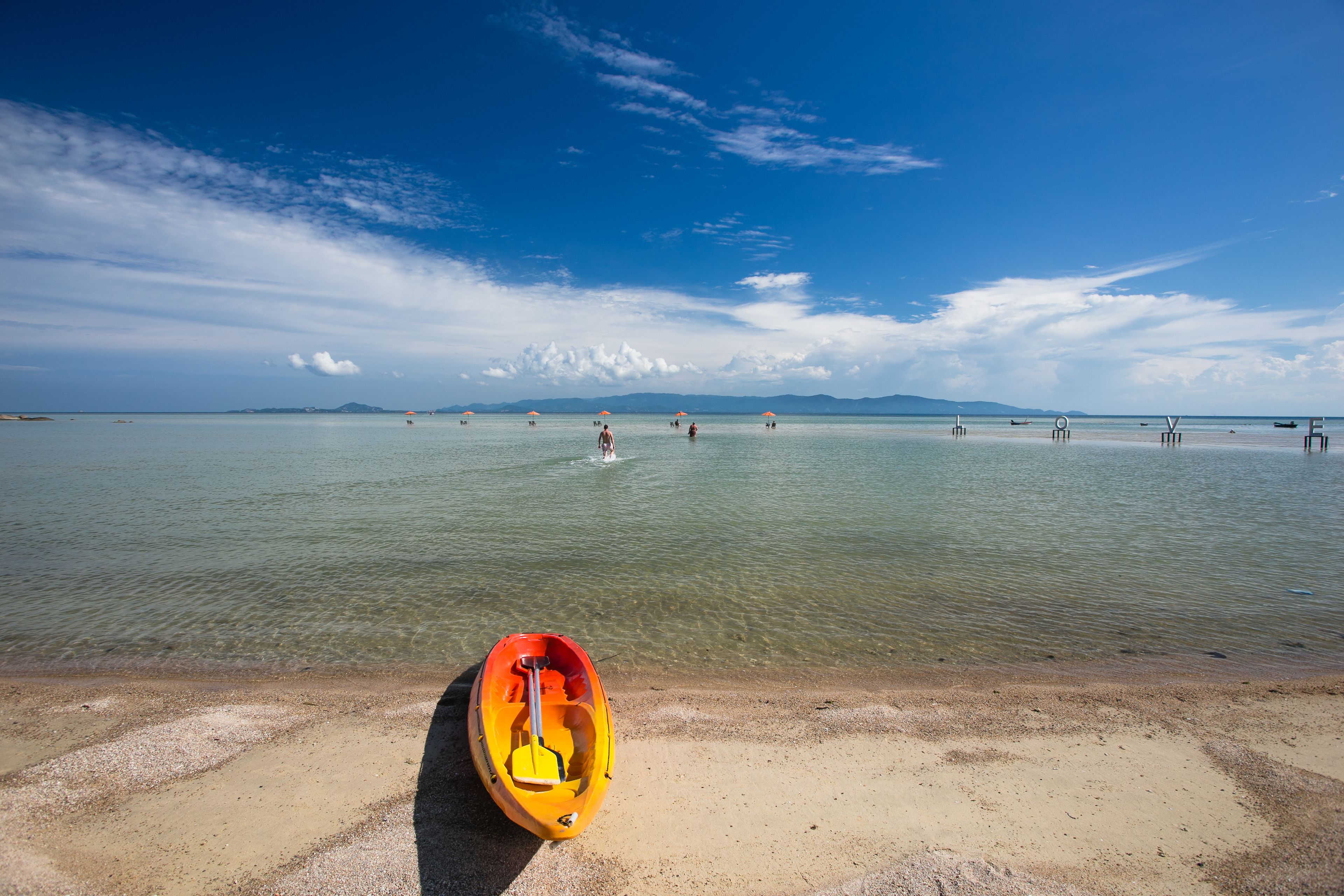 A kayak on a sandy beach with calm water and a clear sky.