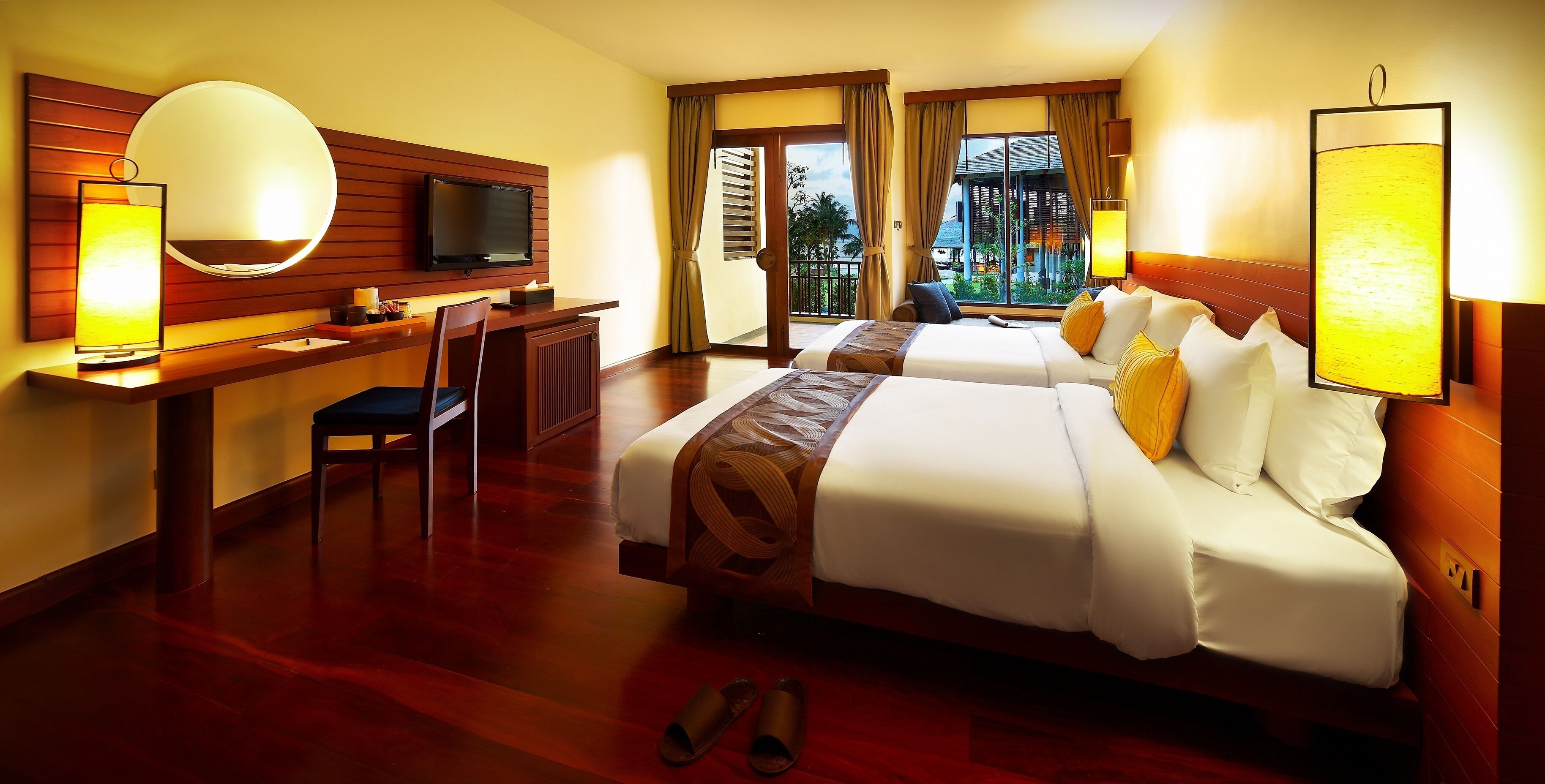 A hotel room with two beds, a desk, a TV, and a balcony with a view.