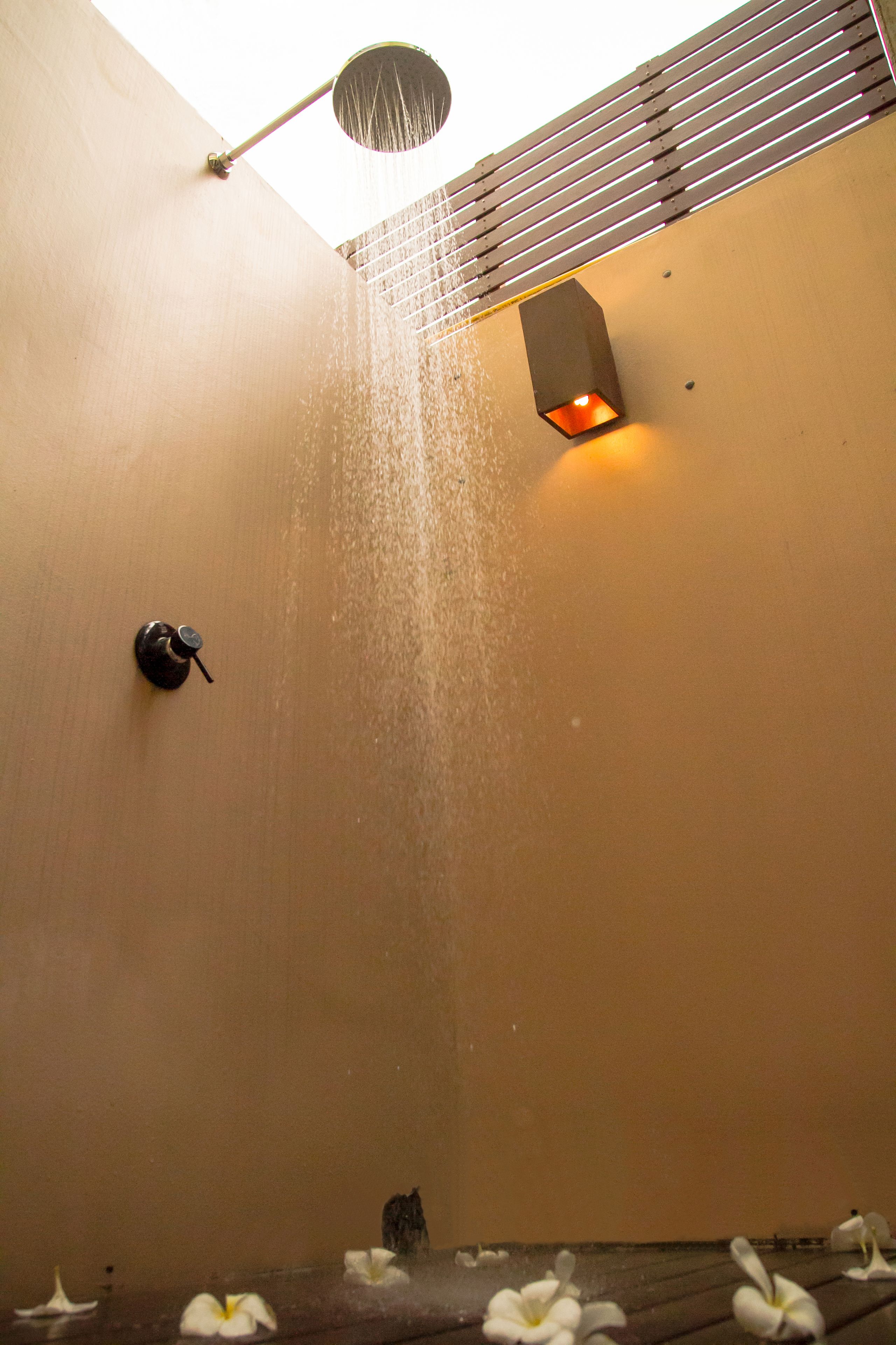 A shower with water falling from the ceiling, a wall-mounted light, and a small window.