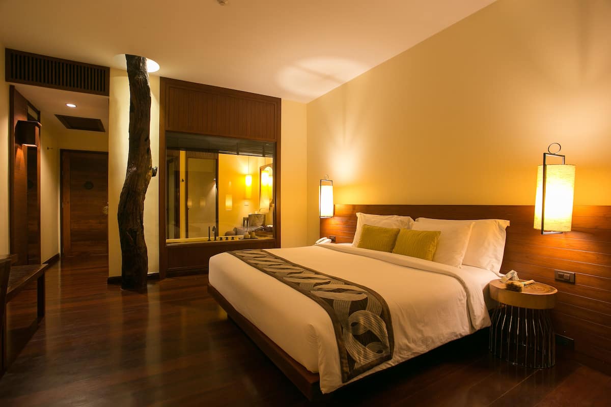 A hotel room with a large bed, wooden flooring, a nightstand, a round side table, and a mirror.