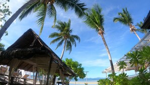 Un resort frente al mar con cabañas de techo de paja, palmeras y una vista despejada del océano.