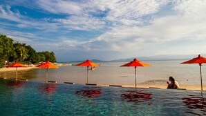 Zona de piscina con agua cristalina, sombrillas rojas y vista a la playa.