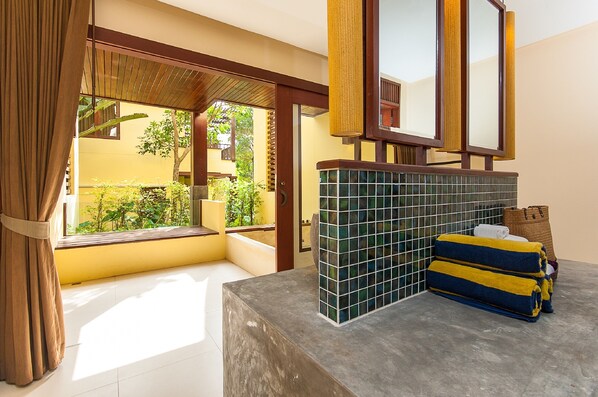 Un baño con lavamanos de azulejos, un espejo y una ventana con cortinas.