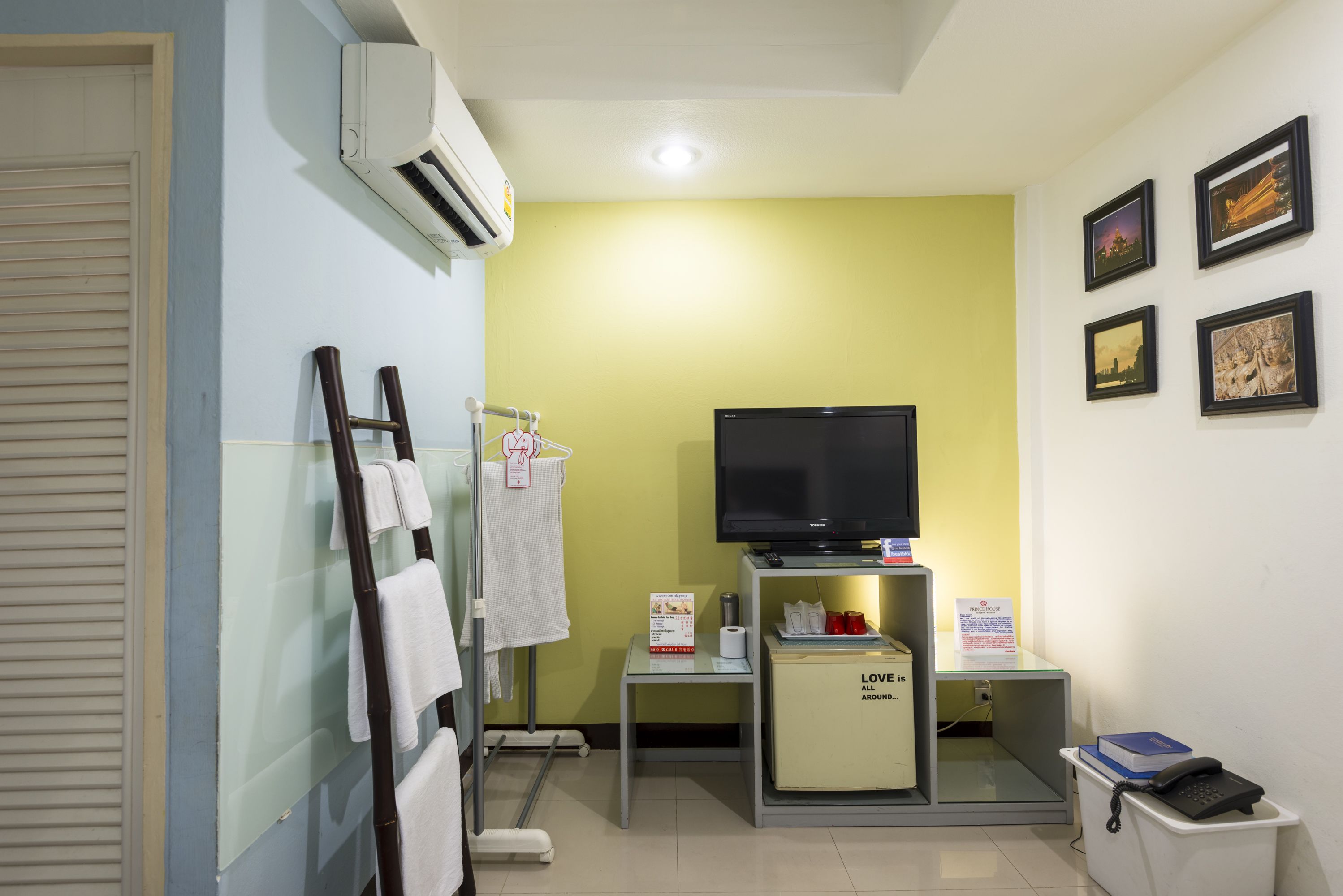 A hotel room with a television, a small table with a sign, a mirror, and a trash bin.