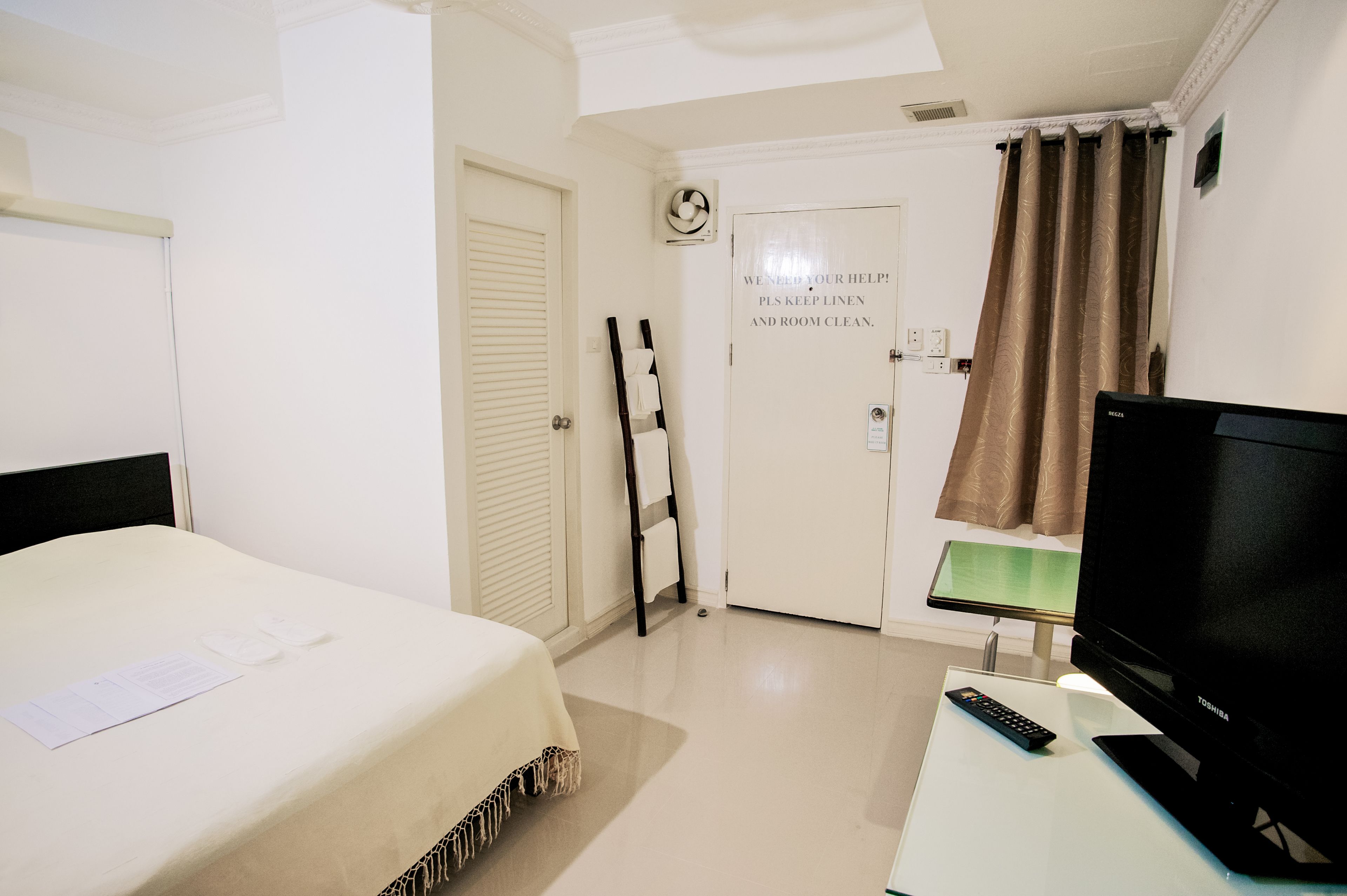 A hotel room with a bed, a desk with a TV, a door with a sign, and a window with curtains.