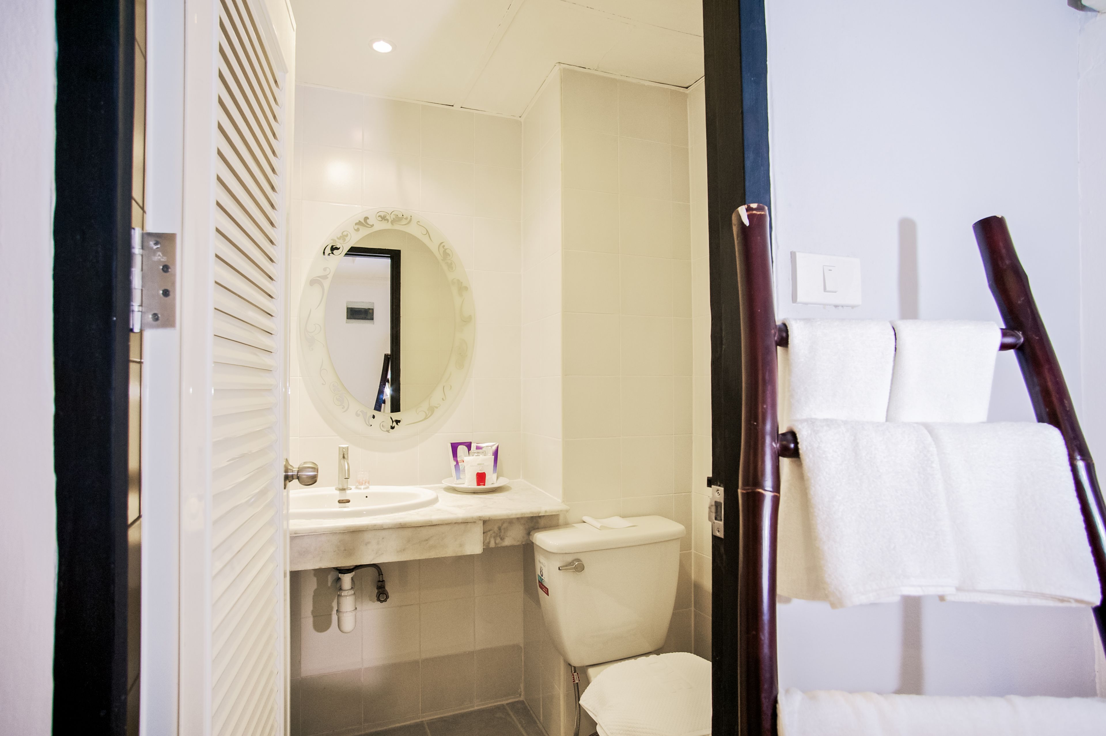 A bathroom with a toilet, sink, and mirror. There is a towel rack with towels.