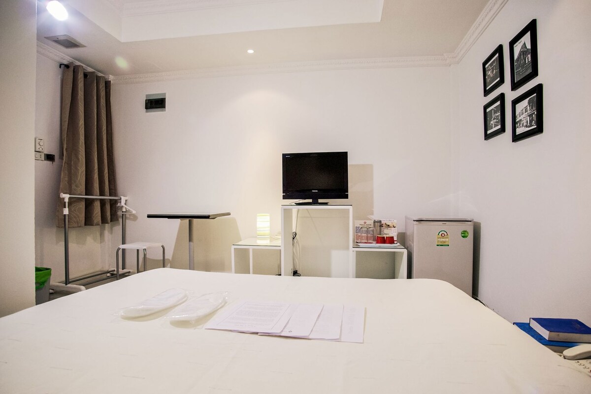 Hotelkamer met een bed, een televisie, een koelkast, een bureau met lamp en een muur met ingelijste foto's.