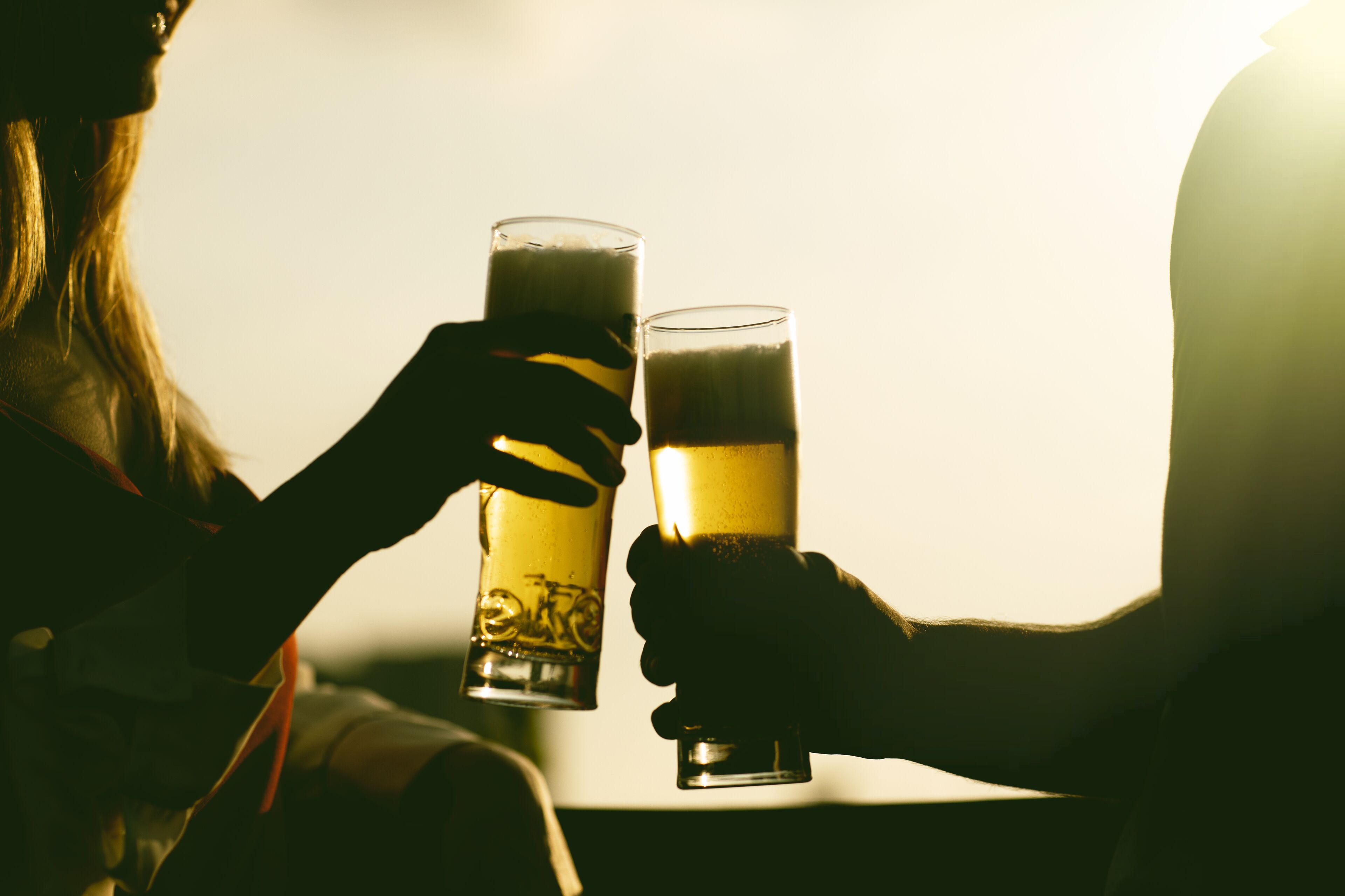 Dos personas sosteniendo vasos de cerveza, probablemente en un ambiente relajado.