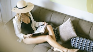 A person sitting on a sofa with a book, wearing a hat, and a jacket. - Marine Heights Suites (Herzliya)