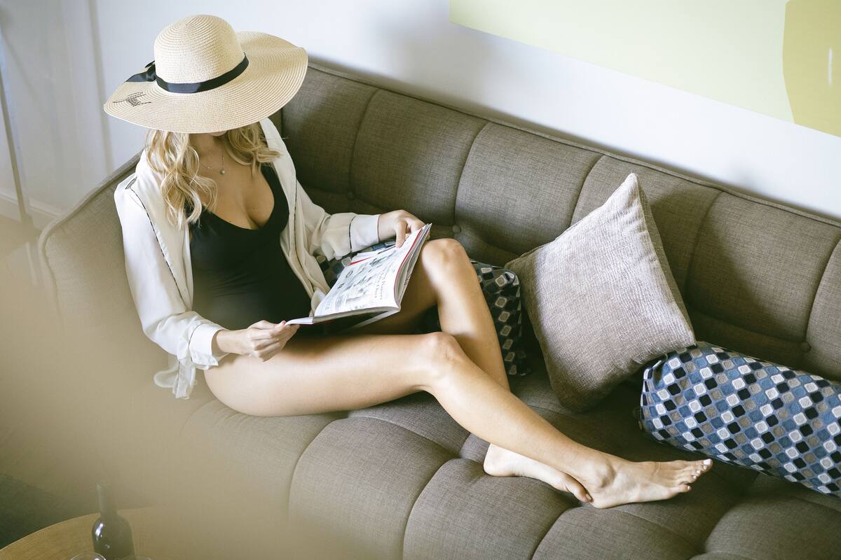 A person sitting on a sofa with a book, wearing a hat, and a jacket.