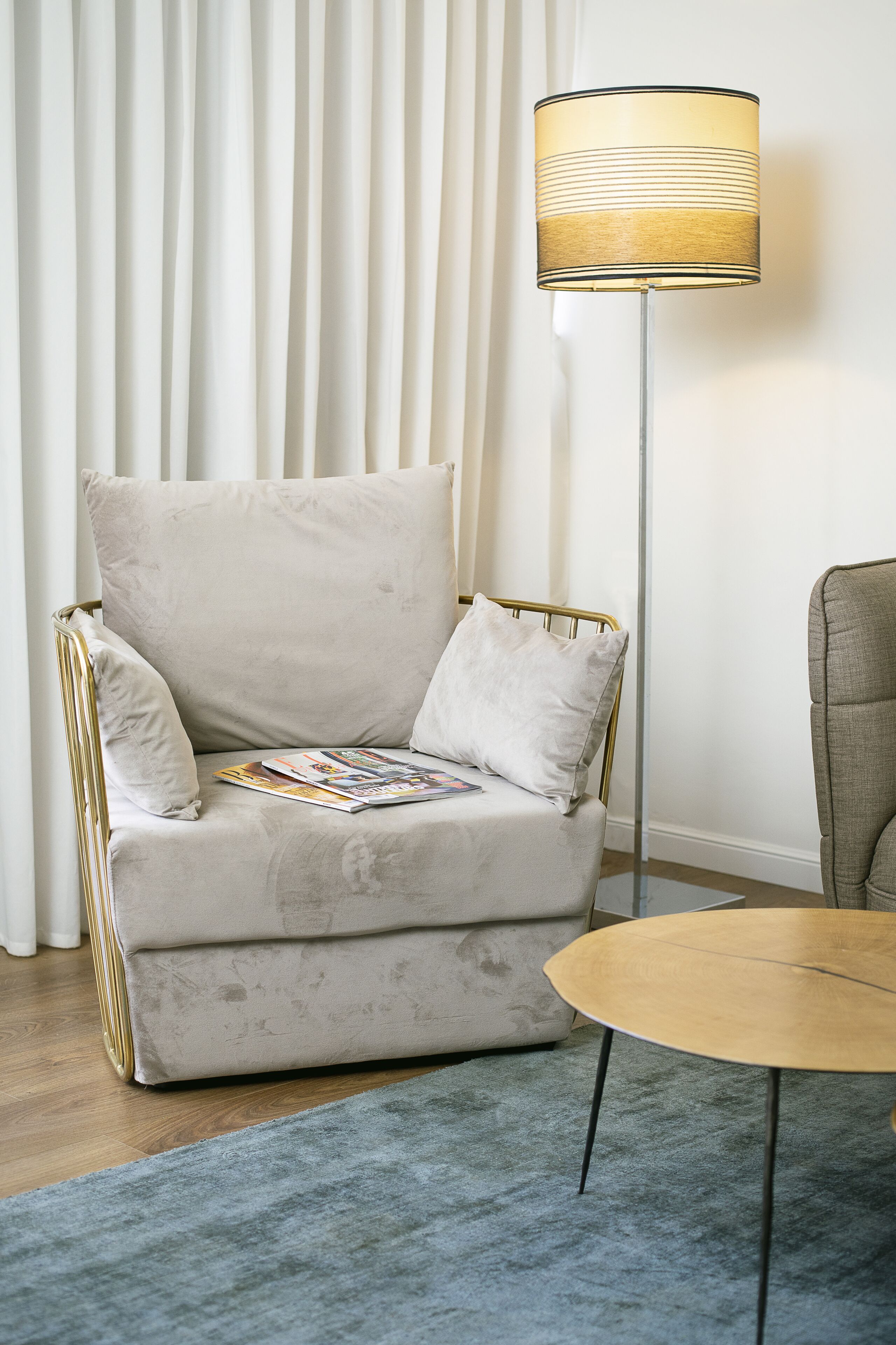 A white armchair with a magazine, a round wooden table, and a floor lamp.