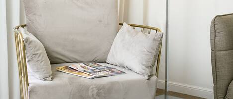 A white armchair with a magazine, a round wooden table, and a floor lamp.