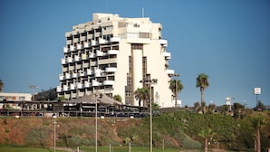 A multi-story building with balconies, located near a beach with palm trees and a pedestrian walkway. - Marine Heights Suites (Herzliya)