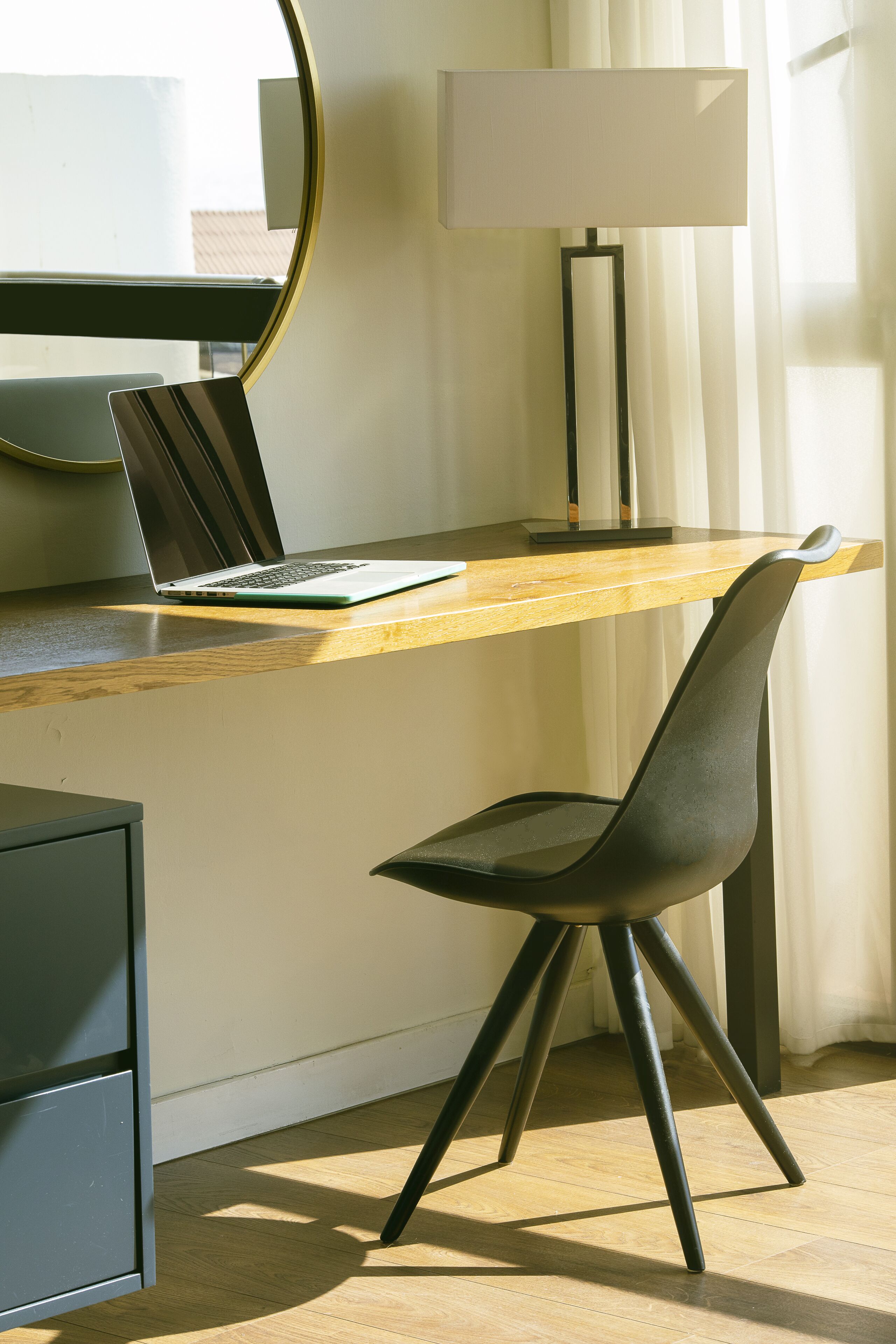 A modern workspace with a laptop on a wooden desk, a black chair, and a floor lamp.