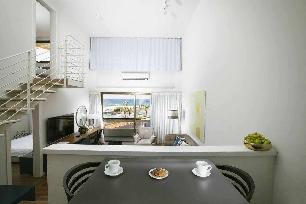 A modern hotel room with a balcony, a dining area, and a view of the sea.