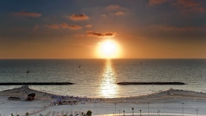A beach with a sunset, calm sea, and a pier with umbrellas. - Marine Heights Suites (Herzliya)