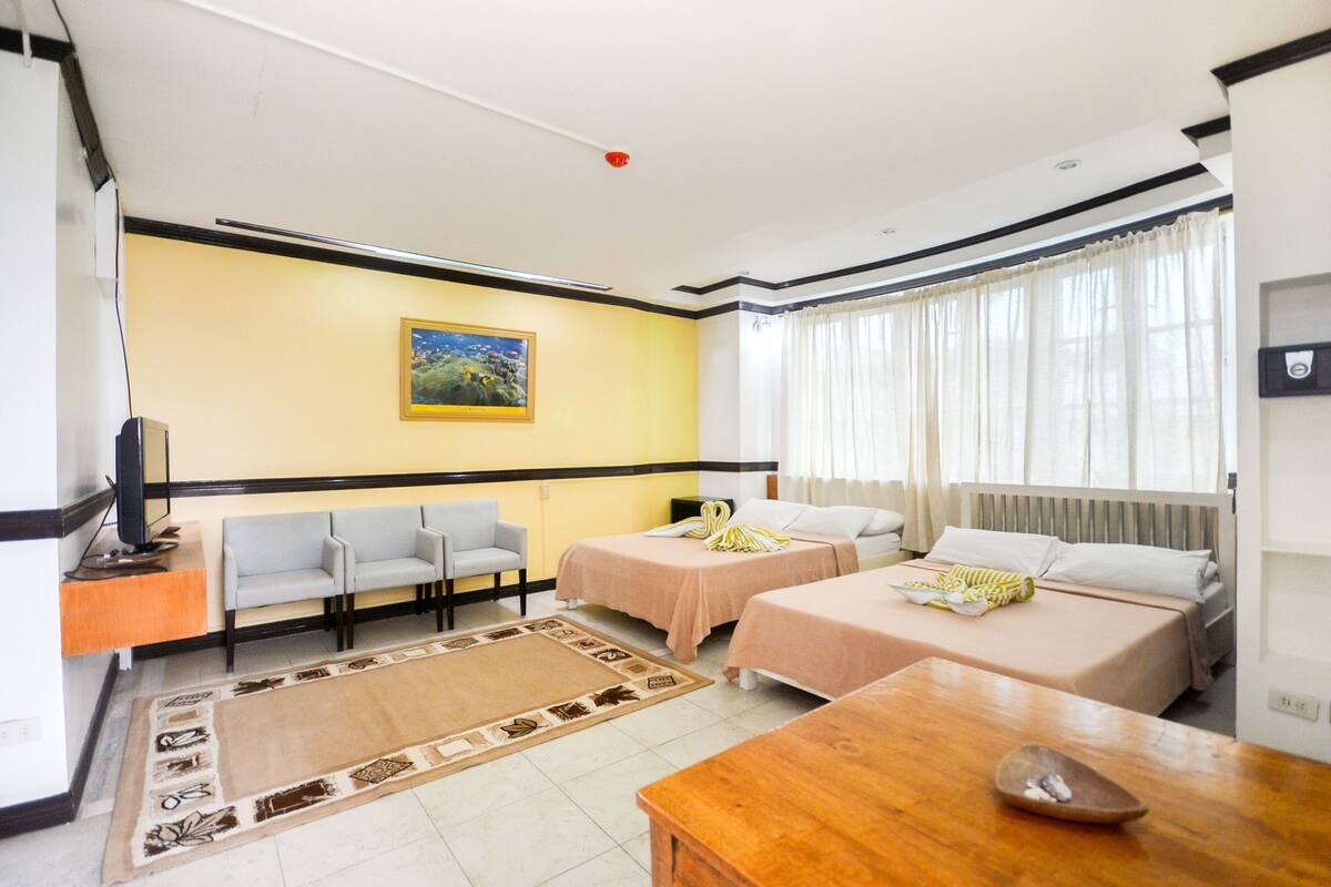 Habitación de hotel con dos camas, un sofá, una mesa de madera y un televisor.