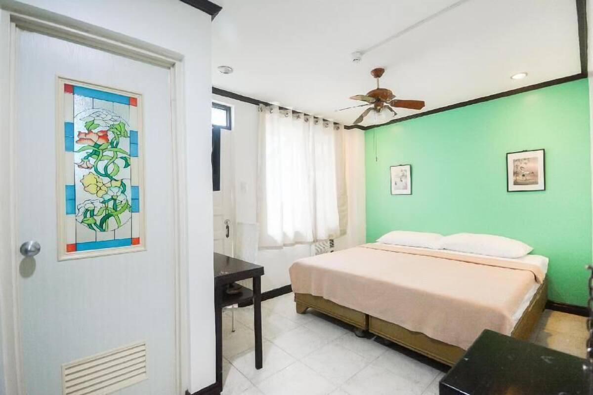 Un dormitorio con cama, escritorio, ventilador de techo y pared verde.