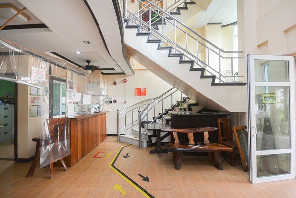 Zona de recepción con una escalera, muebles de madera y una puerta de cristal con un cartel que dice 'ABIERTO'.
