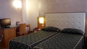 A hotel room with a bed, a desk, a chair, a telephone, and a television.