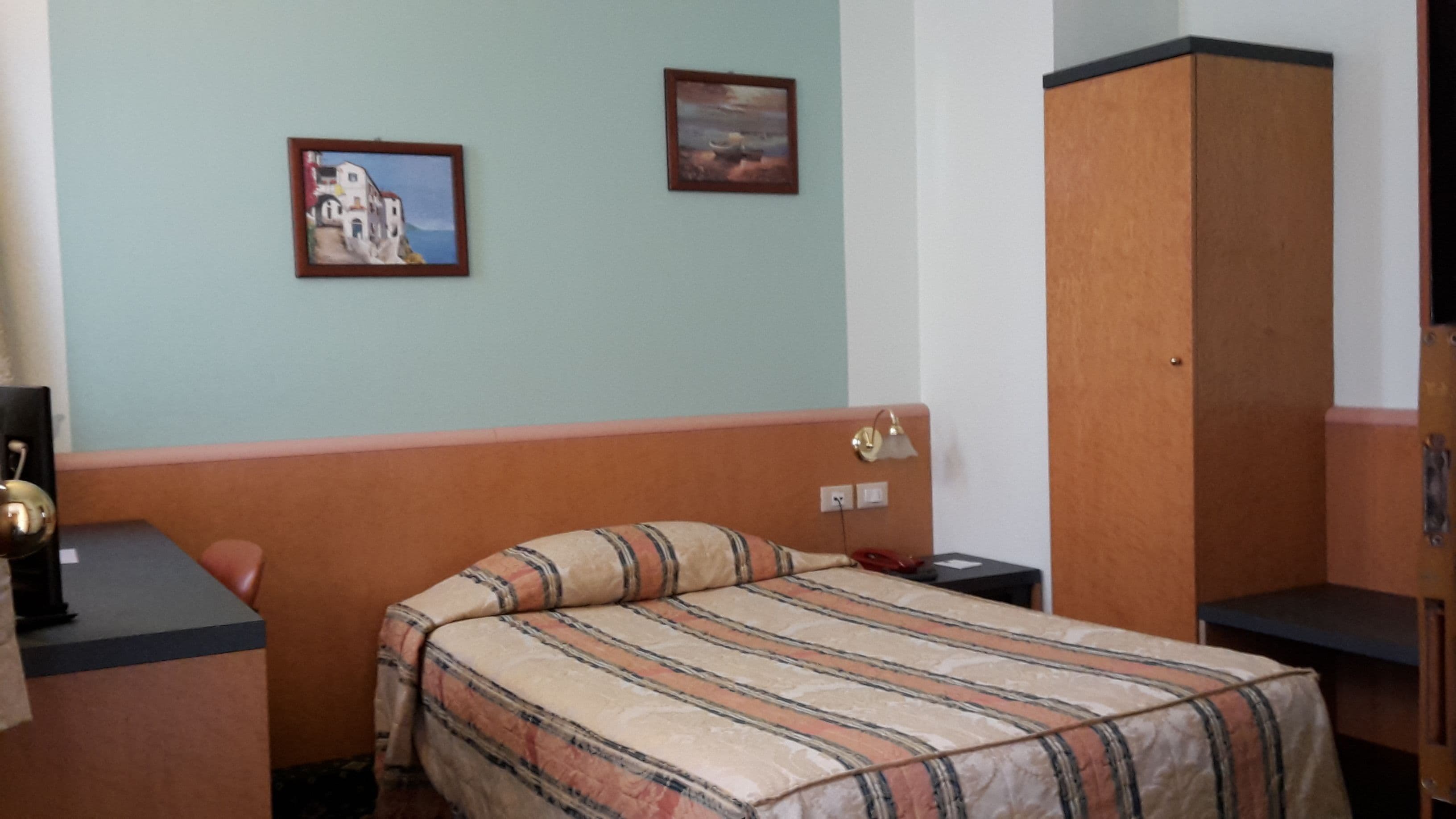 A bedroom with a bed, a nightstand, a wardrobe, and two framed pictures on the wall.
