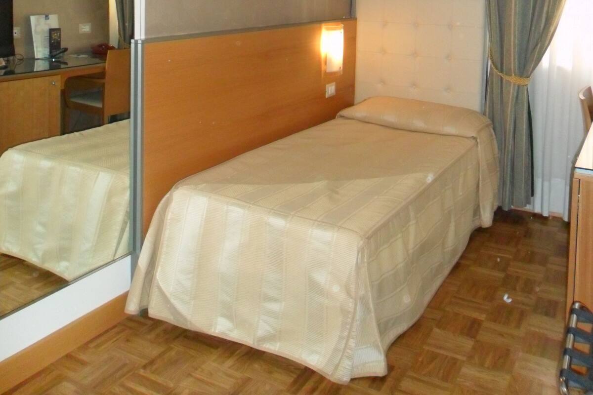 A hotel room with two single beds, a wooden desk, a chair, a mirror, and a window with curtains.