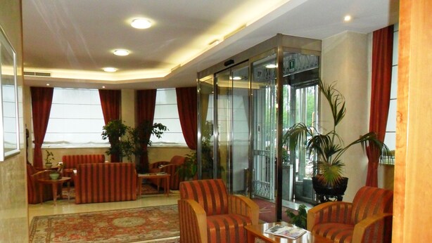 A lobby with striped sofas, a coffee table, and a glass elevator. - Hotel Riviera (Segrate)