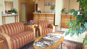 A reception area with a sofa, armchairs, a coffee table with magazines, a reception desk, and potted plants. - Hotel Riviera (Segrate)