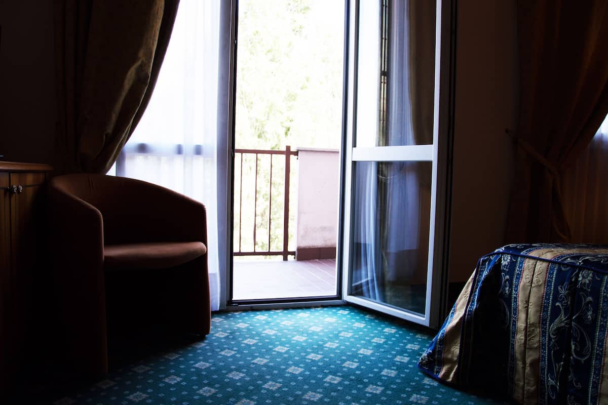 Une chambre dotée d’une porte-fenêtre coulissante donnant sur un balcon, d’une chaise et d’un lit recouvert d’une couvre-lit à motifs.