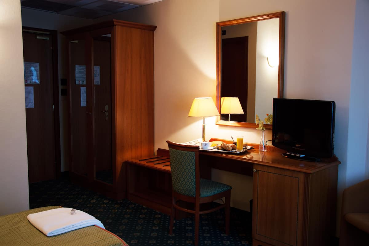 Une chambre d’hôtel avec un bureau en bois, une télévision, une lampe, une chaise et un lit.